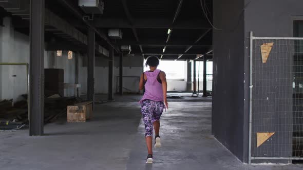 African american woman wearing sports clothing jogging through an empty urban building alt