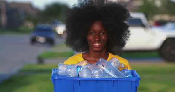 African American adolescents with huge Afro smiling as he hold recycle bin full of plastic bottles alt