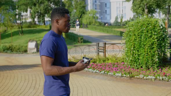 Afroamerican Man Uses Mobile Phone Holding White Cup with Coffee or Tea in Hand alt