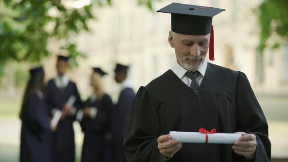 Senior Man in Academic Regalia Holding Diploma, Education at Any Age, New Degree alt