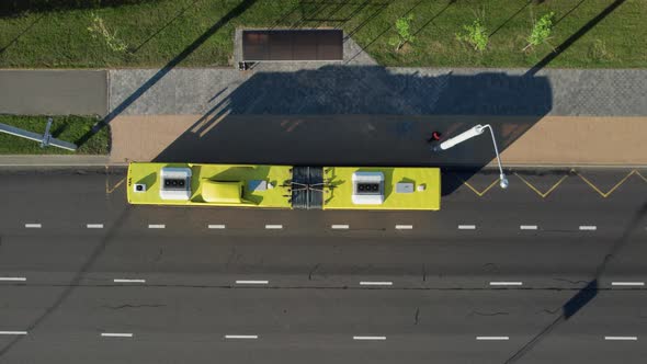 Aerial top view of a yellow city bus pulling up to the bus stop and dropping off passengers. alt