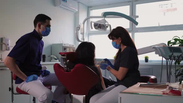 Doctors Dentists Woman and Man in Medical Masks Serve Patient in Dental Clinic alt