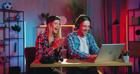Blondie Supporting Her Active Excited Bearded Boyfriend which Playing Video Games on Laptop alt