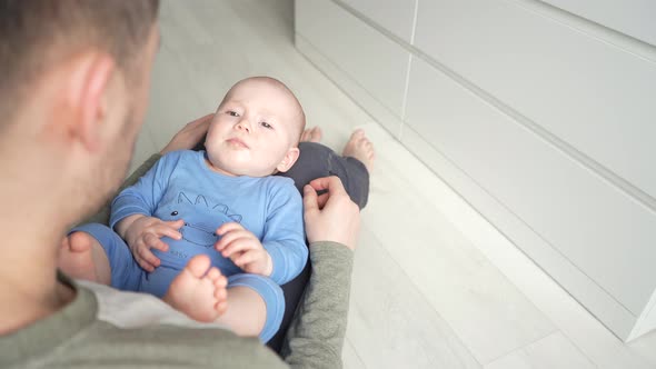 Father Plays with a Smiling Baby Son Lying on Knees at Home Together