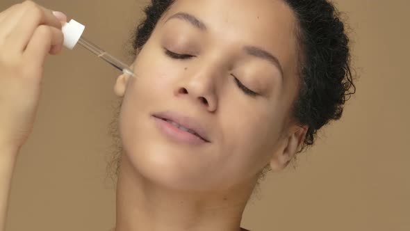 Beauty Portrait Young African American Woman Applying Skincare Serum on Face Rubbing Gently with alt