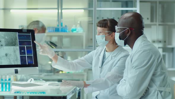 Diverse Colleagues in Masks Discussing Microscopic Image on Computer alt