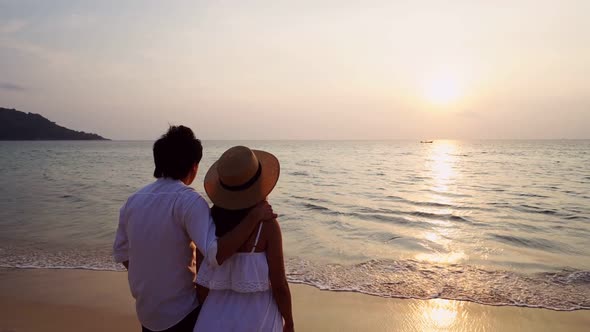 Young asian couple looking beautiful sunset on the beach