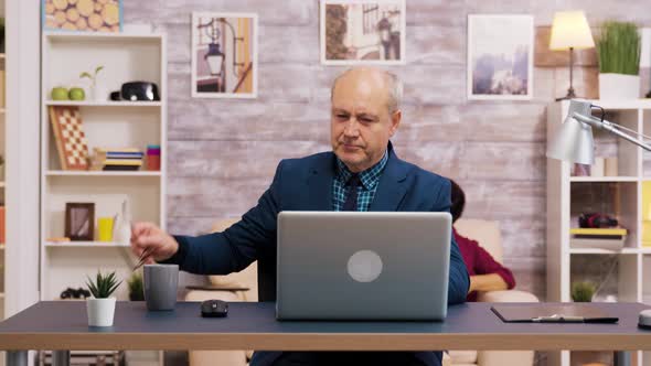 Handsome Old Man Putting on His Glasses While Working on Laptop alt