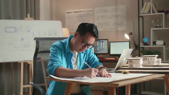 Asian Man Engineer With A Laptop Drawing Blueprint At The Office alt