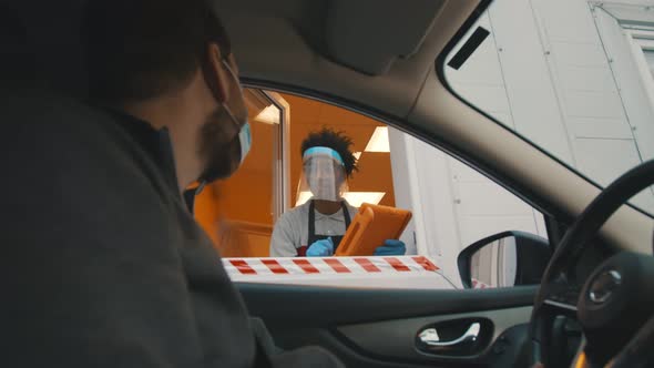Side View of Male Driver in Safety Mask Ordering Meal in Drive Thru Window alt