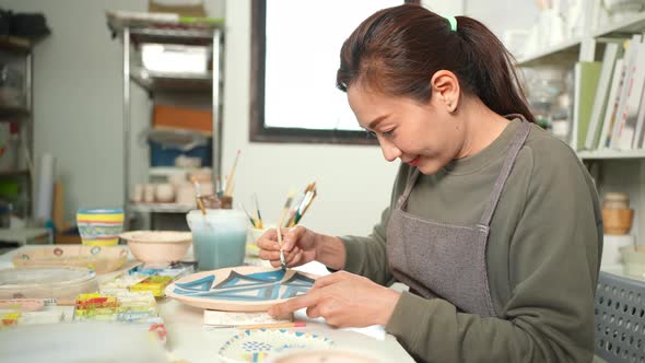 4K Asian woman enjoy painting self-made pottery plate at pottery workshop studio. alt