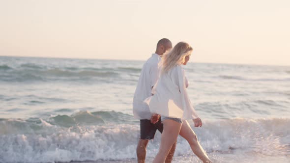 Couple of Young Lovers Holding Hands Walking Along the Beach By the Sea