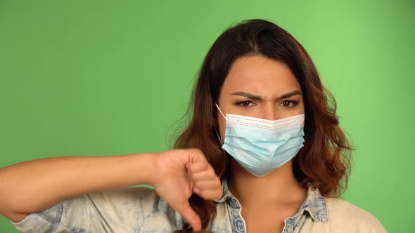 A Caucasian Woman in a Face Mask Shows a Thumb Up and Thumb Down to the Camera   Green Screen