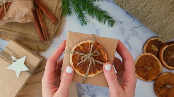 Woman Making Box with New Year's Gifts Wrapped in Craft Paper and Decorated with Dry Orange Slices alt