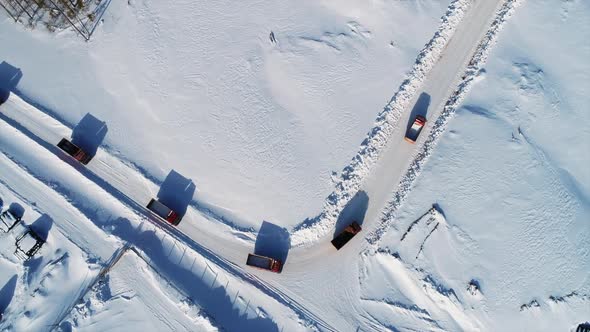 Aerial Shot of Dump Trucks Driving One After Another in Winter on Snowy Road.