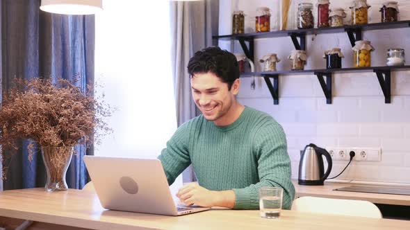 Online Video Chat By Young Man on Laptop Sitting in Kitchen alt