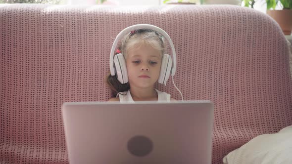 Little Girl Sitting Sofa in Headphones Listen Music Use Laptop Have Fun Home Interior Caucasian alt