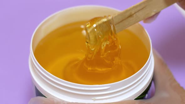 Sugar paste or honey wax for hair removal, dripping from wooden wax sticks - depilation and beauty. alt