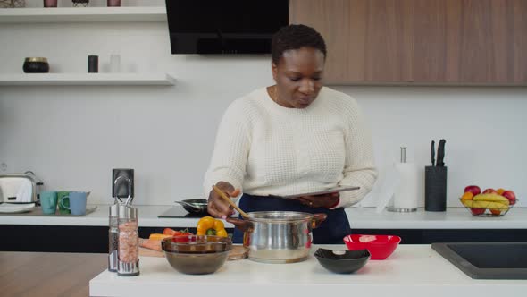 African Woman with Tablet Pc Trying New Recipe at Home alt