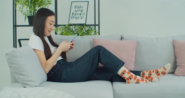 Asian Woman Use Smartphone Application Sitting on Comfortable Sofa Technology Connection Concept alt