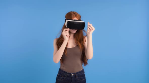 Redheaded Model in VR Headset is Smiling Dancing and Snapping Her Fingers While Posing on Blue alt
