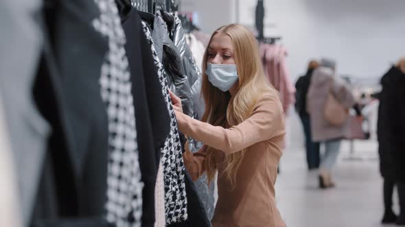 Caucasian Girl in Medical Mask Woman Customer Buyer Looking for Size Color Perfect Autumn Coat alt