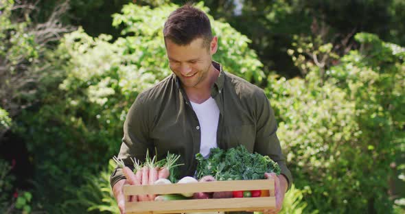 Portrait of caucasian man carrying a wooden tray full of vegetables in the garden alt