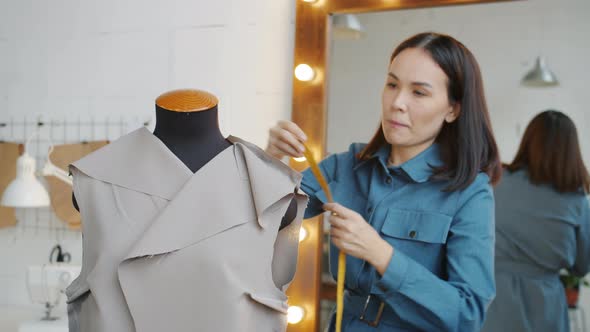 Young Woman Measuring Fabric on Tailor's Dummy Designing New Clothes in Studio alt