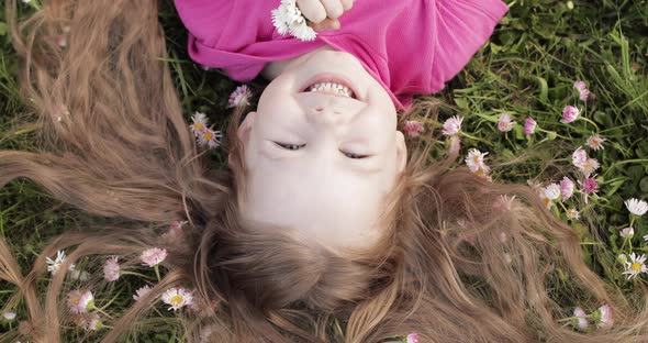 Close-up Smiling Little Cute Baby Girl Lying on Green Grass Holding Flowers Looking at Camera