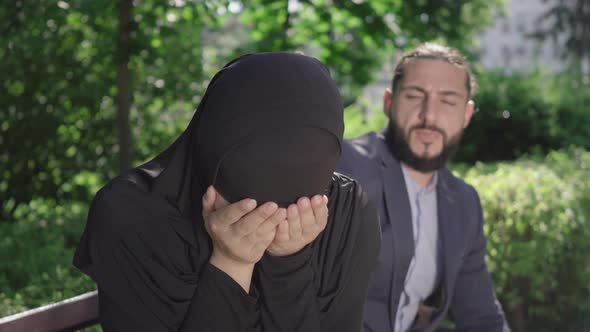 Close-up of Crying Muslim Woman in Hijab Sitting on Bench As Blurred Middle Eastern Man Talking To alt