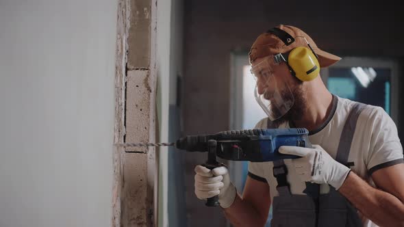 Builder Drilling a Wall with Hammer Drill Wearing Safety Glasses and Headphones