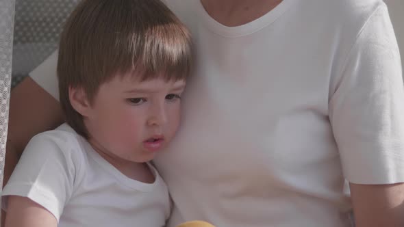 Woman Sits on Window Sill with Cute Toddler Boy on Her Knees. Lockdown Quarantine Because of alt