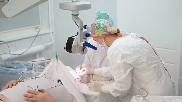 Two Female Surgeons Perform Eye Surgery with Microscope and Medical Instruments alt