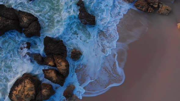 Beautiful aerial drone overhead rotating shot of waves crashing the rocky beach shore alt