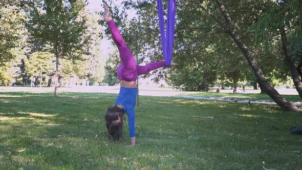 Young Beautiful Sportswear Woman Training Aero Stretch Swing Sunny City Park Hanging Upside Down alt