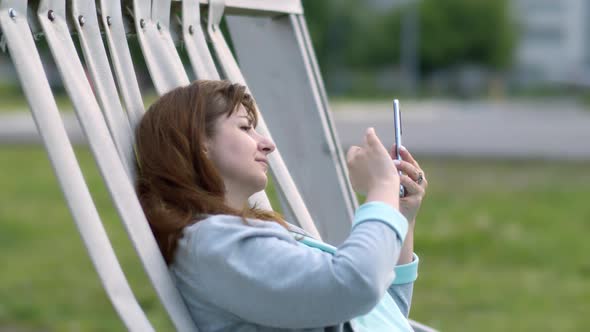Happy Woman Lies in Resting Place and Uses Phone Chat with Friends Read Some Positive Information