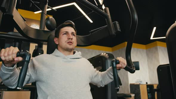 Young Man in Gray Hoodie Training Arms in a Gym