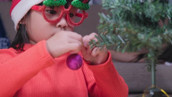 Little girl in Santa hat is decorating the Christmas tree indoors.