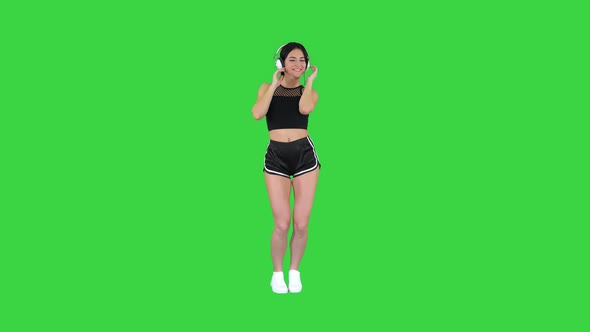 Gorgeous Brunette Lady Listening Music in Headphones on a Green Screen, Chroma Key. alt