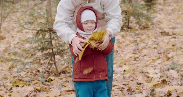 Small Cute Child with His Mother Throws Up Yellow Leaves of the Canadian Maple