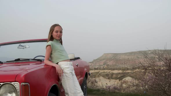 Smiling Happy Girl in White Jeans Stand By Loan Red Convertible Car in Red and Pink Valley in
