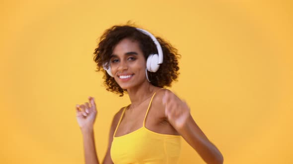Happy African American woman listening to music on wireless headphones and dancing
