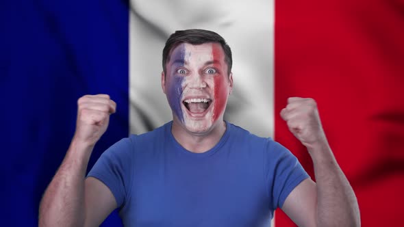 A screaming French cheerleader with a face painted in the color of the French flag.