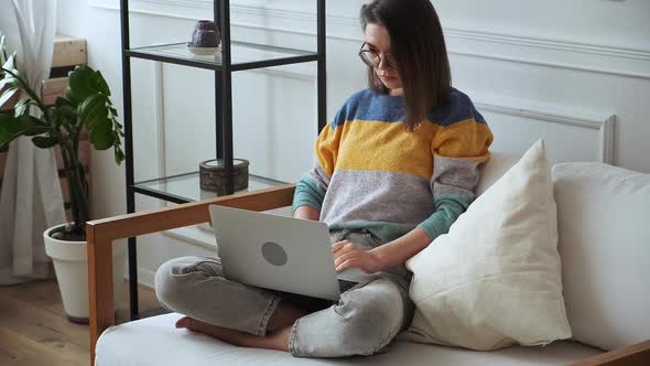 Young Woman Using Laptop Typing Sitting at Home on Sofa Remote Work Work at Home alt