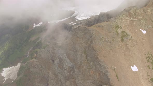 Slow panning look down a mountain top and sheer cliffs onto a meadow and lake below. alt