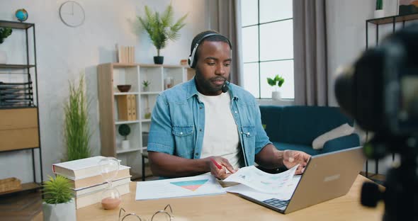 Man in Headset Sitting in front of Camera at Home and Explaining Diagrams alt