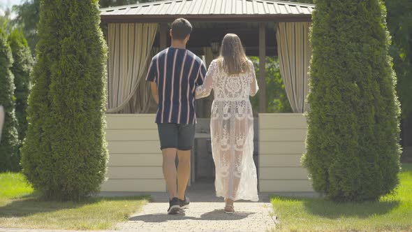 Back View Wide Shot of Young Caucasian Couple Entering Outdoor Cafe at Resort. Confident Brunette alt