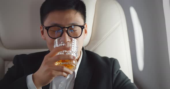 Close Up of Asian Businessman Drinking Whiskey in Glass in Plane alt