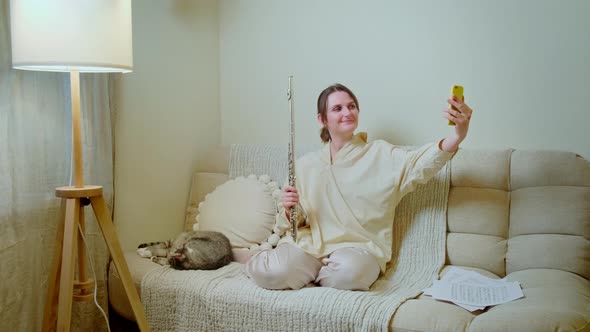 Woman musician with guitar looking at mobile phone at home on sofa in living room alt