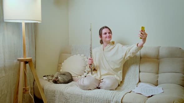 Woman musician with guitar looking at mobile phone at home on sofa in living room